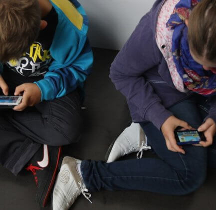 Two kids looking down at their phones screens at school