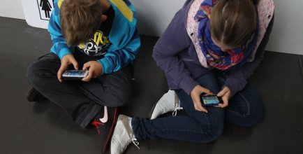 Two kids looking down at their phones screens at school