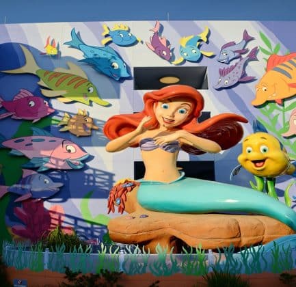 Large colorful mural of Ariel and Flounder from The Little Mermaid, surrounded by animated fish, displayed on the wall of a themed Disney resort building.