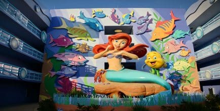 Large colorful mural of Ariel and Flounder from The Little Mermaid, surrounded by animated fish, displayed on the wall of a themed Disney resort building.