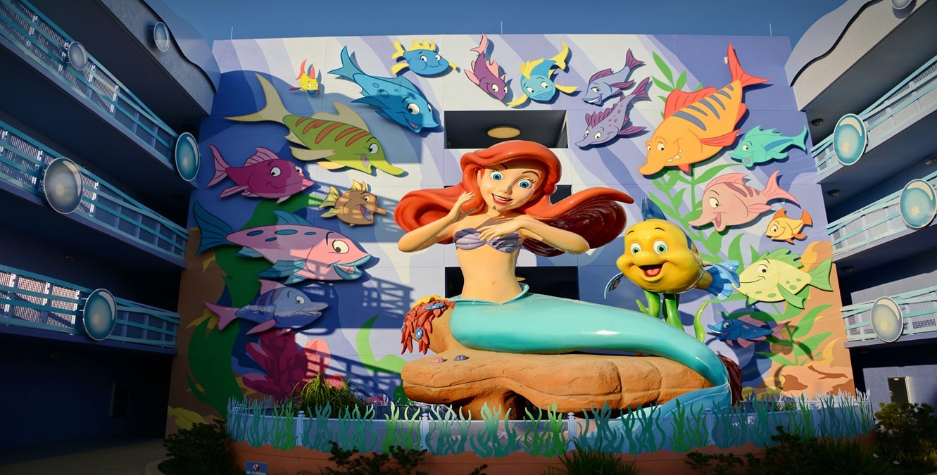 Large colorful mural of Ariel and Flounder from The Little Mermaid, surrounded by animated fish, displayed on the wall of a themed Disney resort building.