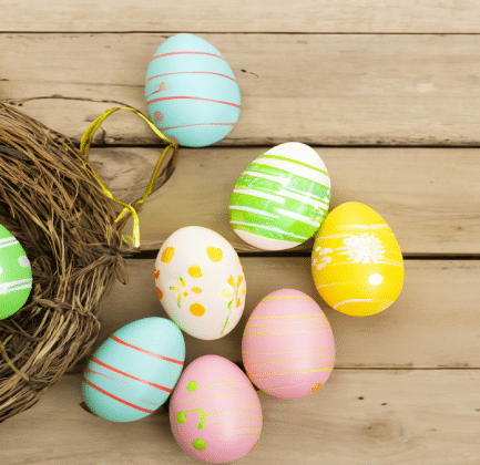 An assortment of colorful eggs in and outside a basket. Representing the question: what came first, the chicken or the egg.
